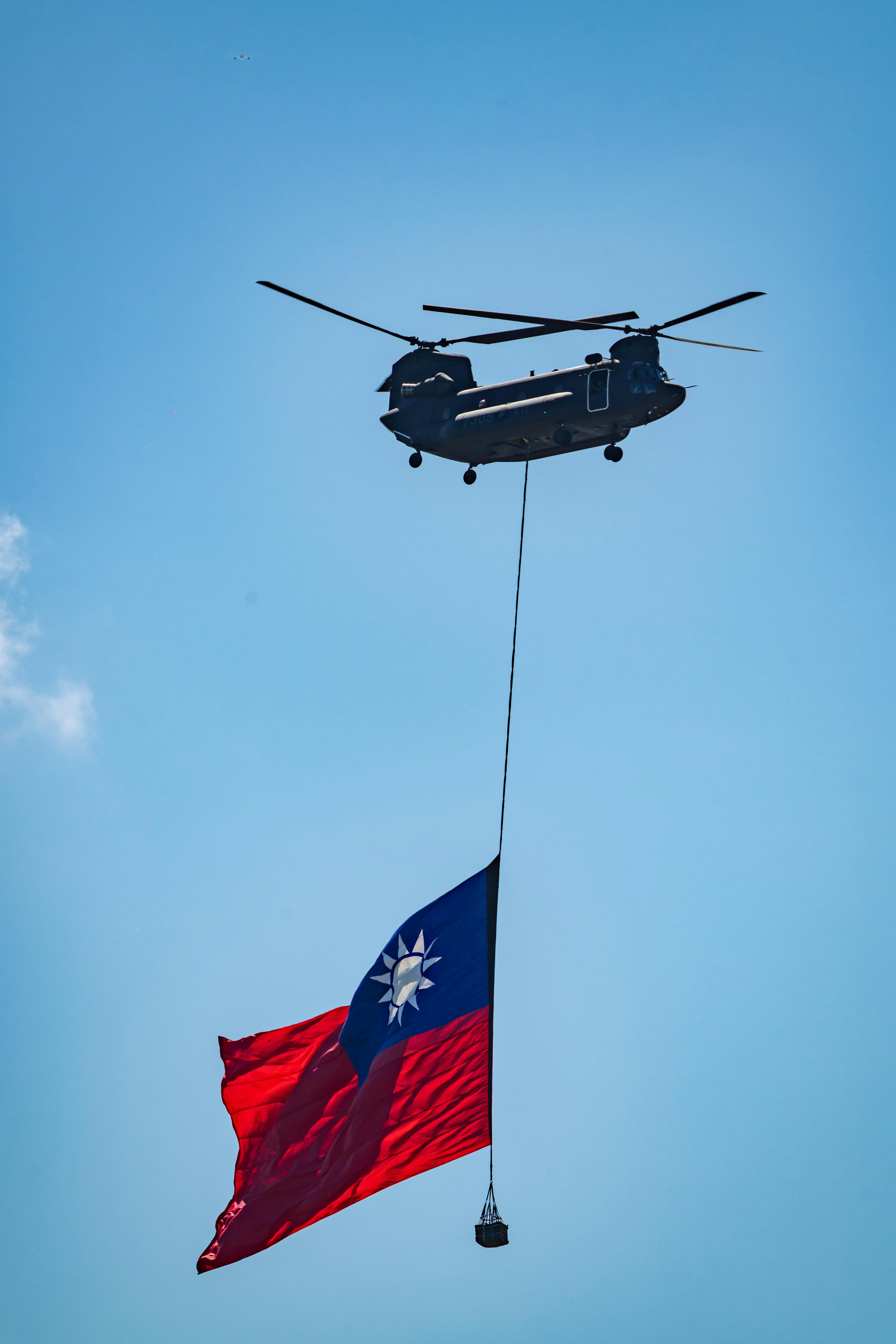 Helicopter flying with Taiwanese flag against a clear blue sky